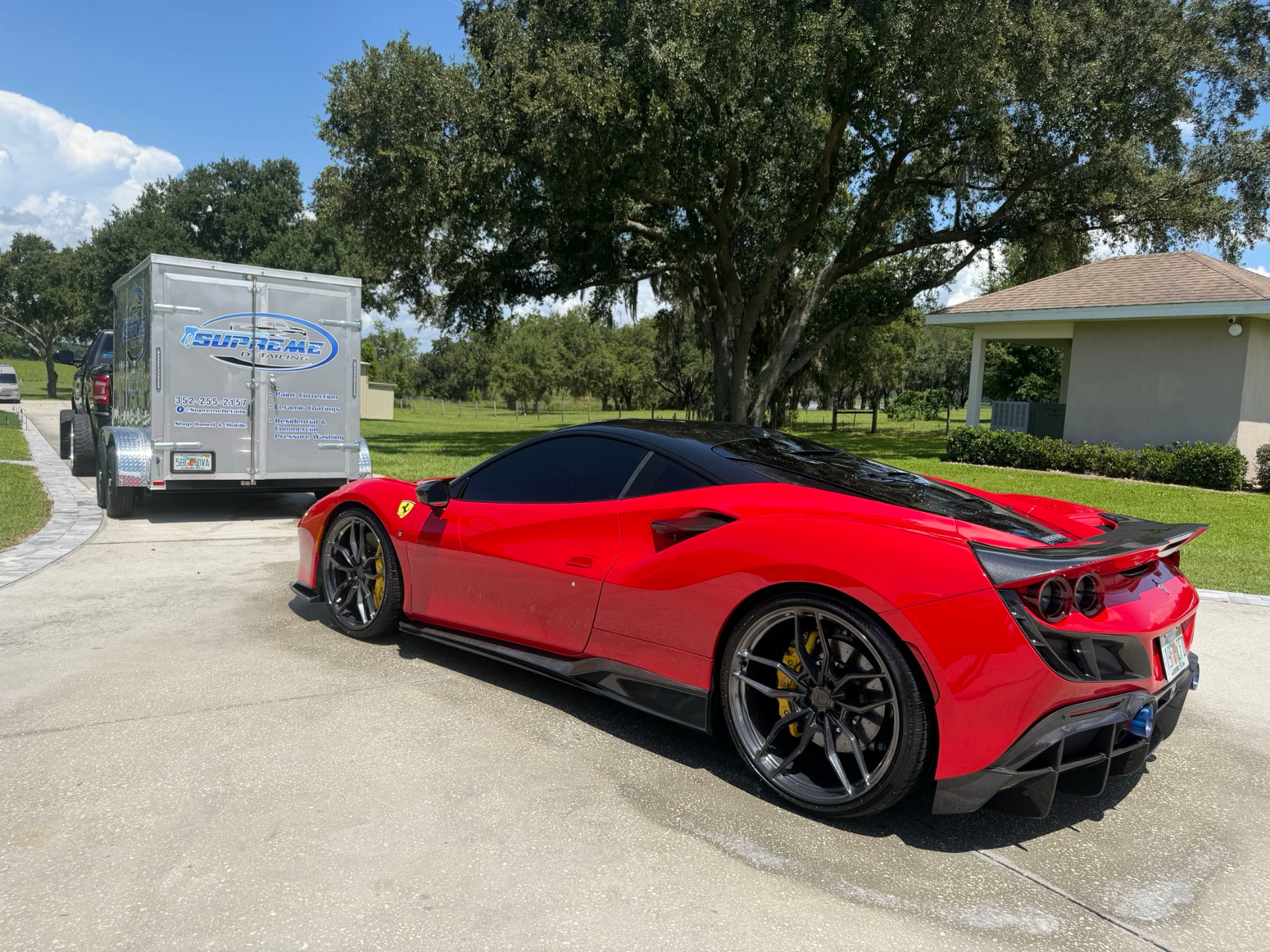 Red Ferrari-style sports car detailed by Supreme Detailing, rear three-quarter view beside the Supreme Detailing trailer